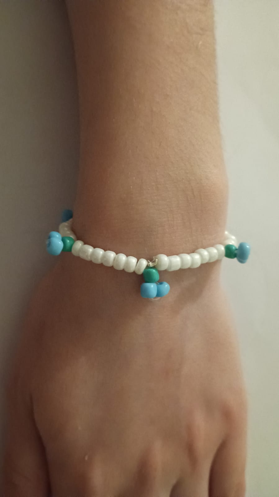Pulsera de cuentas blancas con cerecitas azules, puesta en la muñeca