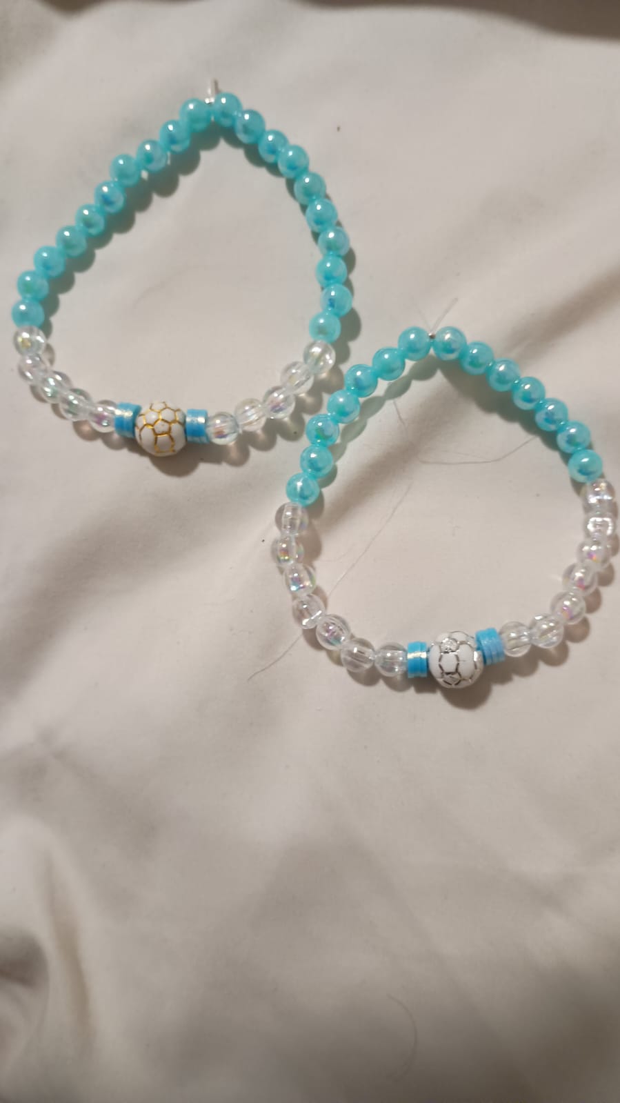 Dos pulseras de cuentas celestes y transparentes con dijes de pelota de fútbol